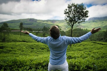 Fototapeta na wymiar Young man with outstretched arms on the background of lush green tea plantations during monsoon