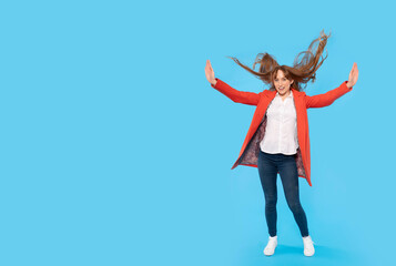 Full body size portrait of an attractive cheerful ginger young woman  jumping, having fun isolated on a blue  background