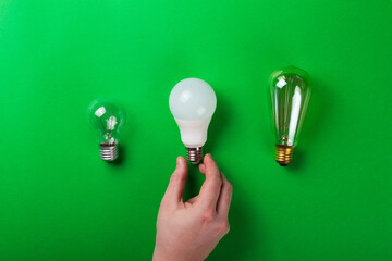incandescent lamp and hand hold led lamps against on isolated green background. Energy efficiency...