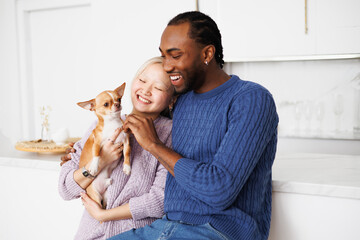 Joyful young diverse couple holding dog and spending time at home