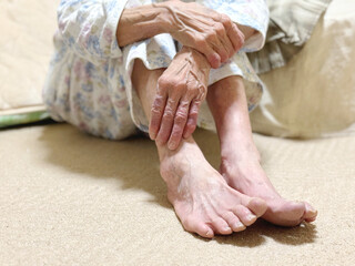 布団の前で寝巻で座る高齢女性の手と足