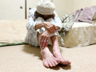 布団の前で寝巻で座ってうなだれる高齢女性