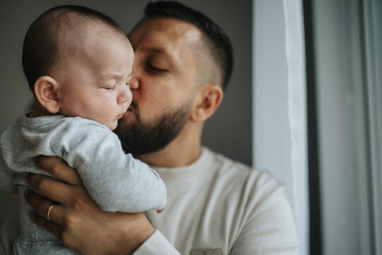 Father kissing cute baby son on cheek at home