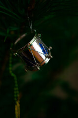 Elegant miniature drum Christmas ornament dangling amidst lush pine needles, capturing the spirit of the holiday season; a detailed festive piece symbolizing celebration and tradition.