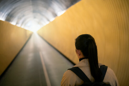 Rear view of woman with backpack walking in subway tunnel