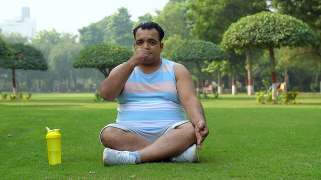 An Indian man doing yoga in the park - healthy lifestyle  fitness journey  pranayam  open public park  alternate breathing
. Unfit man performing respiratory exercise - wearing sportswear  anulom ...