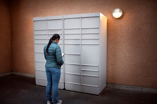 Rear view of woman using smart phone by mail locker