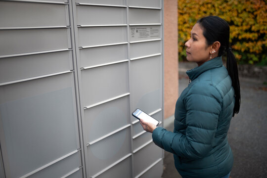 Side view of woman with smart phone looking at mail locker