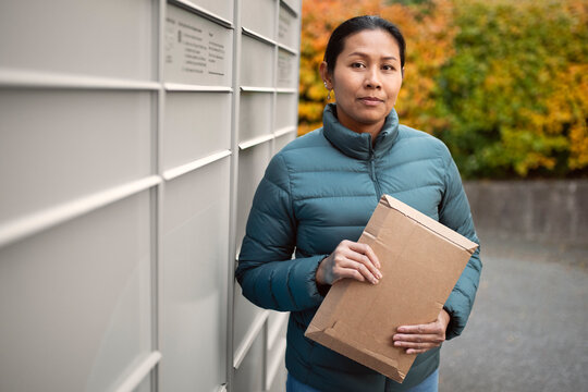 Portrait of mid adult woman with package standing by mail locker