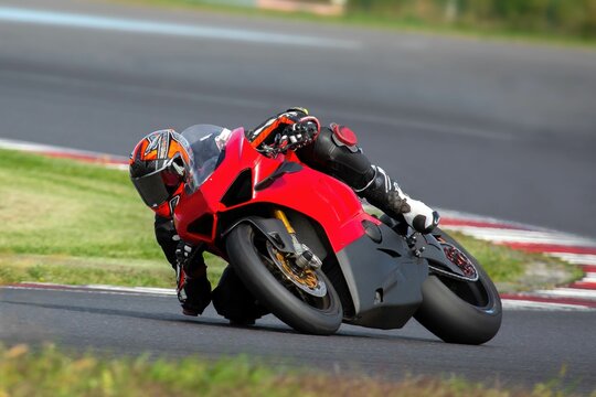 Young adult male is driving a red sports motorcycle on a sharp corner during the race