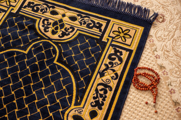 A rosary stands next to a yellow-dark blue and patterned prayer rug,