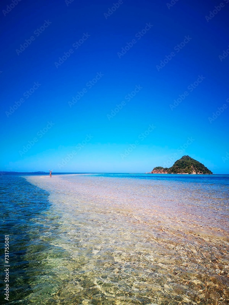 Poster small island in shallow turquoise water with blue sky and beach on the right