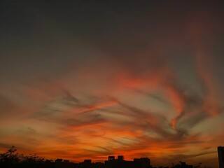 an orange and pink sunset with clouds above the buildings on the skyline