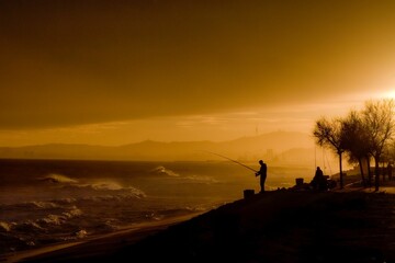 two men fishing on the shore in the evening sun during the day