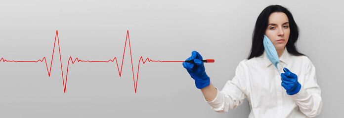 A female hand in a medical glove and a white coat holds a red marker and draws a cardiogram in the...