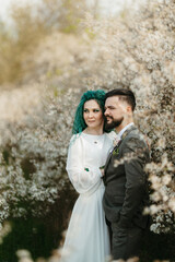 Fototapeta premium a bearded groom plays and a girl with green hair against the background of blooming spring