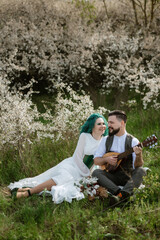Fototapeta premium a bearded groom plays a stringed instrument and a girl sits in a spring meadow