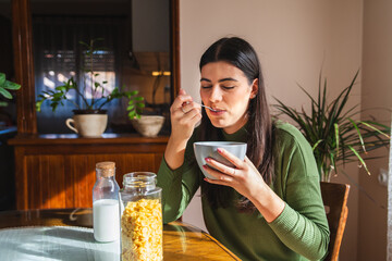 A young woman eating corn flakes for breakfast in the morning in her apartment 