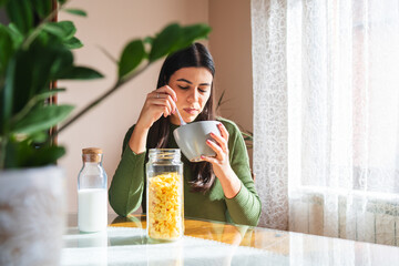A young woman eating corn flakes for breakfast in the morning in her apartment 