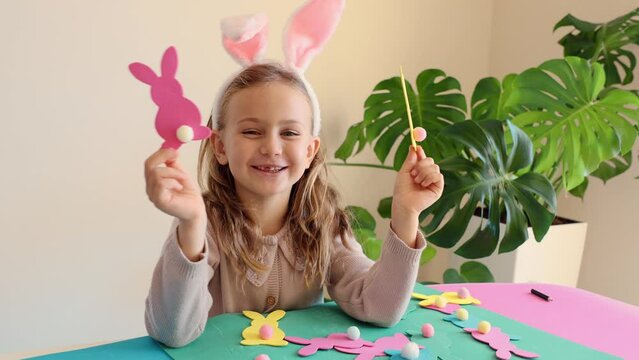 Happy smile excited funny surprised child girl preparing for Easter party make paper garland from colored carton Easter bunny DIY. Happy kids holidays. Toddler in bunny ears costume.