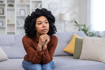 Sad and pensive African American woman sitting sullen at home and suffering from depression, crying...