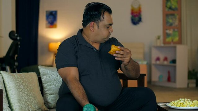A fat Asian man exercising with a dumbbell and eating fast food - temptation to eat  unhealthy food  fired food  unsaturated fats. An Indian man eating an oily samosa and exercising - weight loss  ...