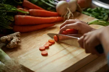 Fototapeten Vegetables, hands and person with knife and carrot cut and for cooking lunch and nutrition diet at home. Wellness, health and organic food with meal, vegetarian and ingredients for salad in a kitchen © peopleimages.com