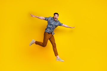 Fototapeta na wymiar Full length photo of childish funky man dressed print shirt brown trousers flying hold arms like wings isolated on yellow color background