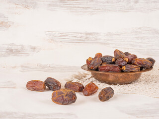 Group of palm date fruits, side view close up image group of palm date fruits. Copper bowl top of white lace cover. White rustic wooden background. Copy space. Ramadan Iftar food, appetizers.