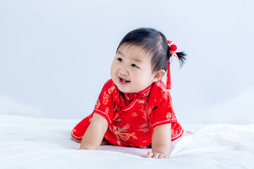 Chinese New Year concept, cute happy little girl in Chinese dress sitting in white living room. Cute Asian baby sitting in white living room, Chinese New Year concept.