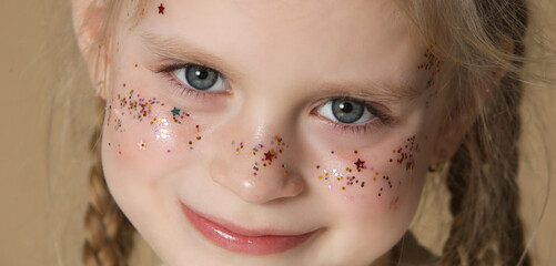 Portrait of cute little blonde girl with blue eyes and glitters on her face.
