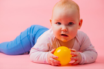 Portrait of a baby girl on a pink background with a yellow ball