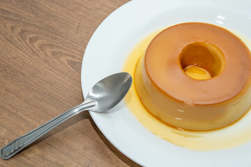 pudim de leite, or pudding also known as flan on a wooden table with metallic spoon