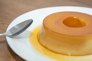 pudim de leite, or pudding also known as flan on a wooden table with metallic spoon