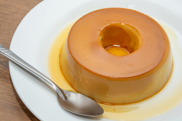 pudim de leite, or pudding also known as flan on a wooden table with metallic spoon
