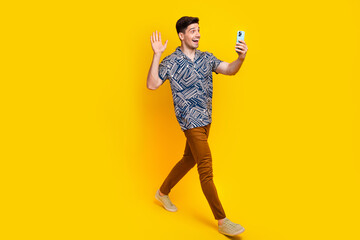 Full length photo of cheerful man dressed print shirt pants say hi at smartphone talk by video call...