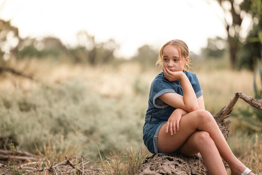 Portrait of pre-teen girl sitting on log in natural setting with thoughtful expression