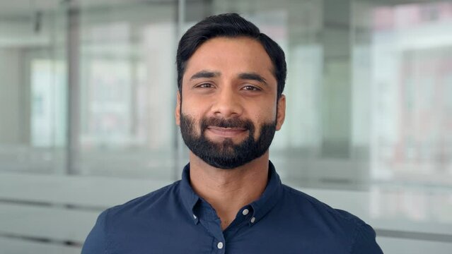 Happy bearded Indian business man leader looking at camera standing in office hallway. Professional smiling businessman manager executive or male employee or entrepreneur headshot portrait.