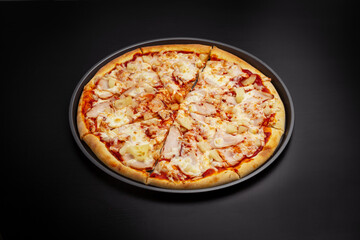 Hawaiian pizza with chicken, pineapples and cheese. On a black background.