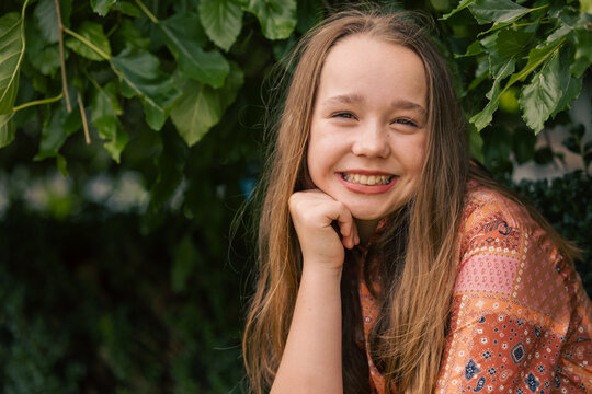 Portrait of pre-teen girl sitting on brick wall with natural green leafy background