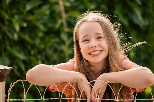 Portrait of cheerful pre-teen girl leaning on wire fence in country town