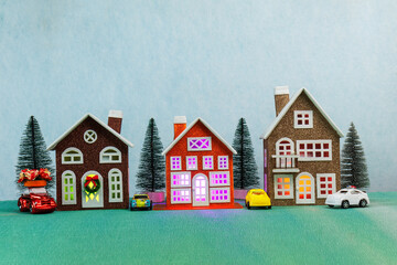 On a light blue background, three large multi-colored houses with Christmas trees and cars near them