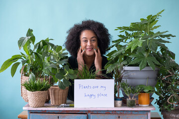 Studio portrait of smiling woman surrounded with plants with sign in foreground