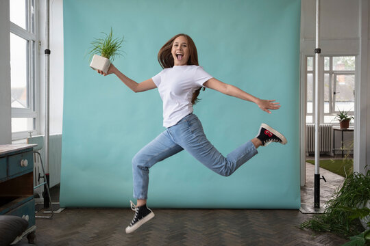 Studio portrait of teenage girl jumping with small potted plant in hand