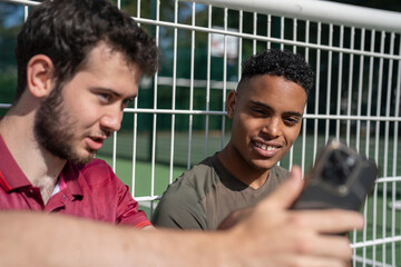 Two smiling men sitting on pickleball court, looking at smart phone