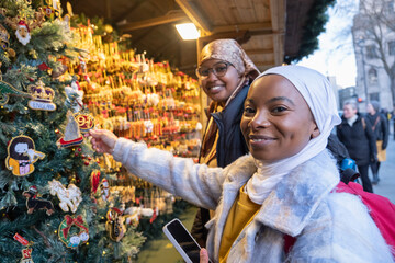 Young female tourists in hijabs buying decorations in Christmas market