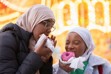 Young female tourists in hijabs eating donuts - obrazy, fototapety, plakaty