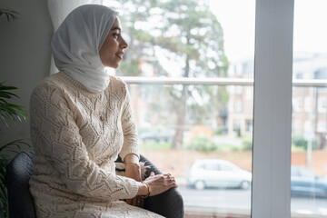 Smiling woman in hijab sitting in chair at home
