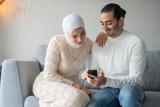 Mid adult couple sitting on sofa and using smart phone