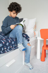Boy (6-7) sitting on bed and reading book